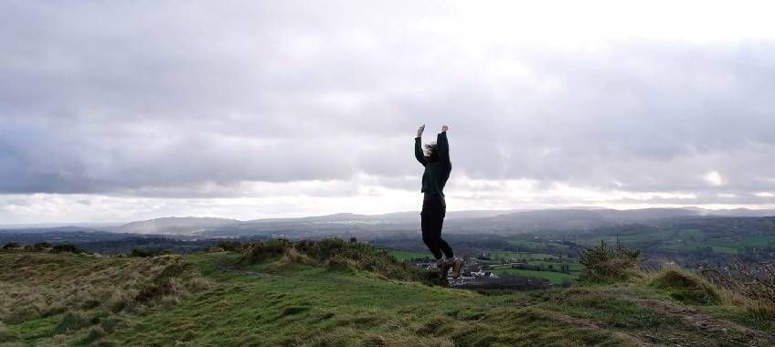 A woman jumps for joy on a hilltop